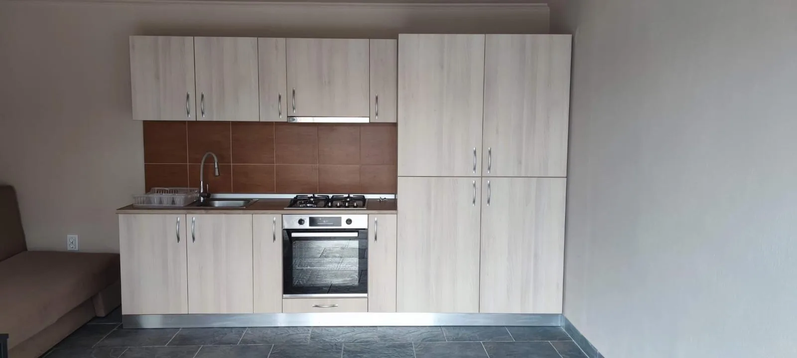 Bucătărie dreaptă în decor stejar deschis cu spate maro și coloană de depozitare, pentru garsonieră